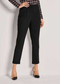 Zwarte op maat gemaakte broeken met een rechte snit, met zijzakken en opgerolde manchetten. Gecombineerd met zwarte en transparante hoge hakken.