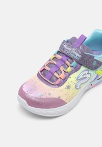 O sneaker sportiv multicolor are un superior sclipitor de culoare purpurie, șireturi elastice și o talpă albă netedă cu modele de stele.