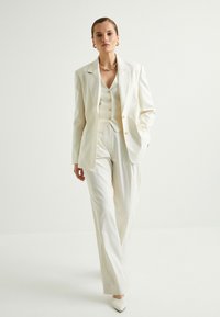 Conjunto de traje blanco a rayas que consiste en una chaqueta, chaleco con botones y pantalones de pierna ancha. Tejido suave con un diseño estructurado y un ajuste a medida.