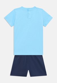 Ανοιχτό μπλε βαμβακερό μπλουζάκι με κοντά μανίκια και δύο κουμπιά στο πίσω μέρος, συνδυασμένο με σκούρο μπλε βαμβακερά σορτς με ελαστική μέση.