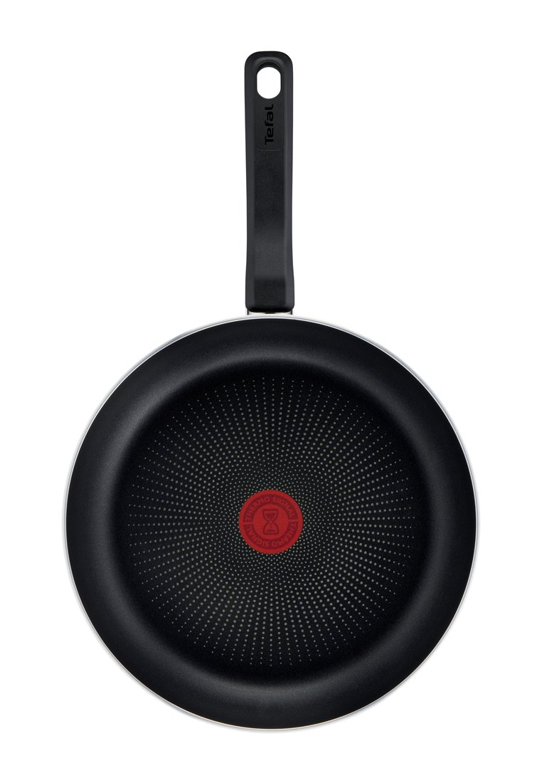 Antihaft-Bratpfanne mit einem flachen, schwarzen Körper, strukturierten Oberfläche mit kleinen Punkten und einem roten zentralen Indikator. Schwarzer ergonomischer Griff.