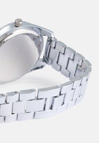 Relógio de aço inoxidável prateado com bracelete liso e brilhante e caixa redonda. Apresenta uma coroa texturizada e um design elegante.