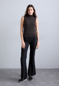 Brun ärmlös polotröja kombinerad med höga svarta utsvängda byxor. Svarta loafers med vita sulor. Slät, åtsittande tyg.