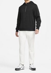 Svart fleecehoodie med halvdragkedja och ribbade ärmslut, i kombination med vita slim-fit byxor och svart-vita sportskor.