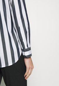 Randig skjorta med marinblå och vita vertikala ränder, knappade manschetter med kontrasterande randdetalj, tillverkad av lättviktig tyg.