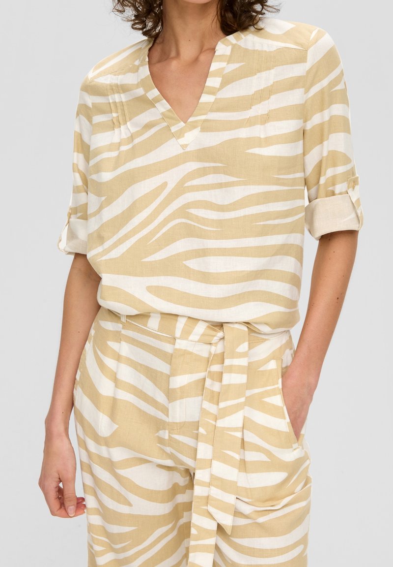 Blusa in lino a righe beige e bianche con scollo a V e maniche corte arrotolate. Abbinata a pantaloni coordinati con cintura legata.