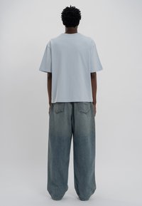 Světle modré tričko s krátkým rukávem a volným střihem, spárované s volnými, vybledlými modrými džíny s mírným gradientem a zadními kapsami.