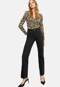 Čierne plisované džínsy v kombinácii s béžovým topom s dlhým rukávom, ktorý zdobí čierny leopardí vzor. Modelka má na sebe čierne lodičky.