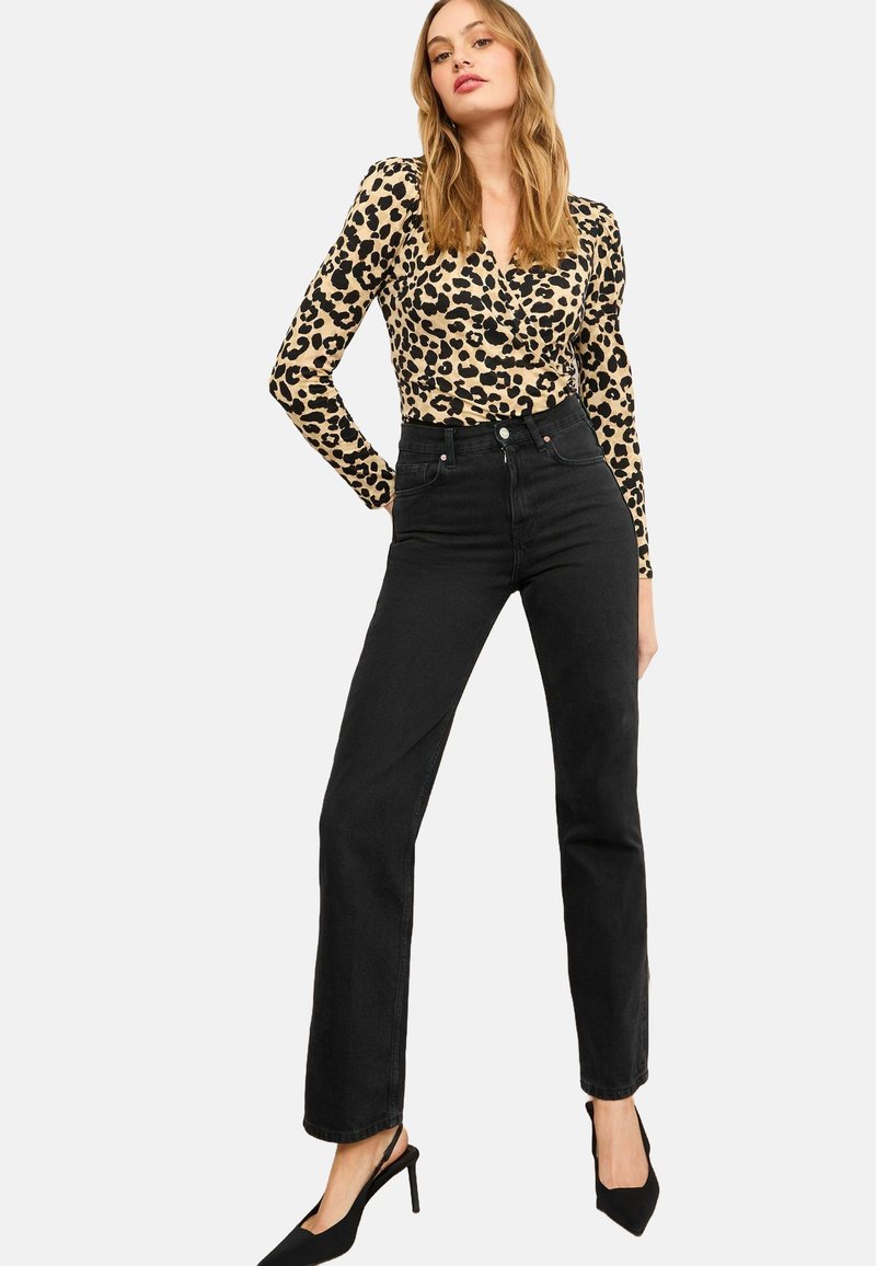 Zwarte high-waisted jeans gecombineerd met een beige long-sleeve top met een zwart luipaardpatroon. Het model draagt zwarte hakken.
