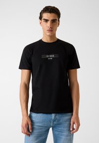 Zwart katoenen T-shirt met een centraal "GUESS"-logo en daaronder "EST. 1981", ronde halslijn, korte mouwen en een aansluitend model.