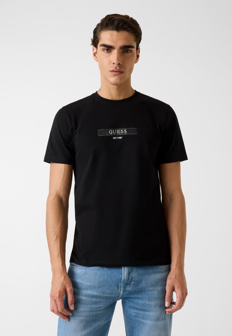 Zwart katoenen T-shirt met een centraal "GUESS"-logo en daaronder "EST. 1981", ronde halslijn, korte mouwen en een aansluitend model.