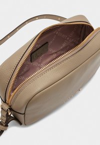Beige lædertaske med en glat overflade, guld lynlås og et mønstret indre. Har en skulderrem og en mærke-logo tag indeni.