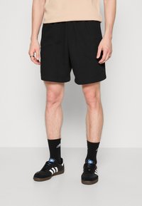Black athletic shorts with a textured fabric, featuring an elastic waistband and side pockets. Worn with black socks and black shoes.