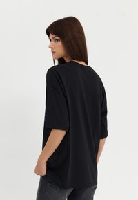 Black oversized t-shirt, short sleeves, round neckline, smooth texture, featuring graphic detail on the sleeve, paired with dark jeans.