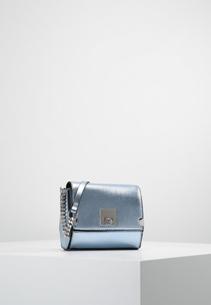 Petit sac à main bleu métallique avec bandoulière chaîne argentée et fermoir carré argenté, posé sur un socle blanc sur un fond uni.