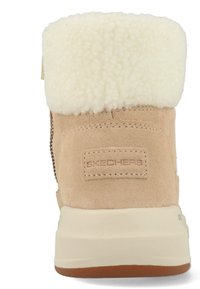Beige suedeboot met een fluffy witte nepbont kraag, voorzien van een zijrits en een gestructureerde rubberen zool met een bruine accent.