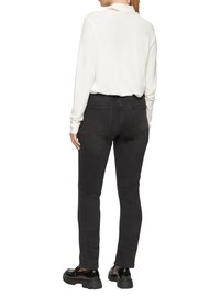 Zwarte jeans met een slim fit en achterzakken, gecombineerd met een witte langemouwen top met een uitsnede achteraan. Zwarte schoenen.