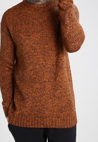 Pull texturé dans un mélange orange-brun, avec un col rond et un ourlet côtelé. Conçu avec des manches longues et une coupe décontractée.