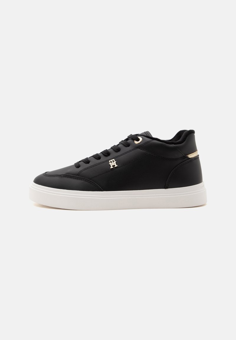 Μαύρο sneaker χαμηλής κοπής με μαύρα κορδόνια, λευκή σόλα και μικρό χρυσό μεταλλικό λογότυπο στο πλάι, εμφανίζεται από την εξωτερική πλευρά.