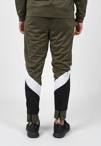 Khaki jogger kalhoty s panelovými vzory v bílé a černé barvě. Mezi vlastnosti patří zipové manžety a texturovaný povrch látky.