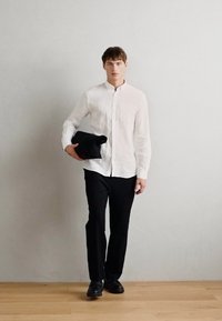Camisa de linho branca com botões, calças pretas ajustadas, segurando uma bolsa de roupa preta. Textura suave, design ajustado, linhas limpas.
