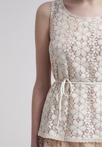 Lace peplum top in cream, featuring floral cutouts, a drawstring waist, and a textured finish around the neckline and hem.