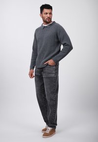 Grå ribbad stickad tröja med krage, kombinerad med blekta svarta jeans och ljusbruna sneakers med vita snören. Stående pose framför en neutral bakgrund.