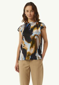 Mehrfarbige Bluse aus fließendem Stoff mit Rundhalsausschnitt, kurzen Ärmeln und abstrakten Mustern in Blau-, Braun- und Schwarztönen.