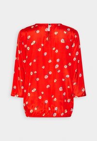 Blusa de satén rojo con mangas tres cuartos, que presenta un patrón floral en rosa y blanco, un escote en forma de ojo de cerradura en la parte posterior y un dobladillo fruncido.