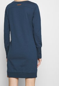 Pulovrové šaty v námořnické modři z bavlněné směsi, s dlouhými rukávy, kulatým výstřihem a žebrovaným lemem. Na zadní straně se nachází malá kožená etiketa.