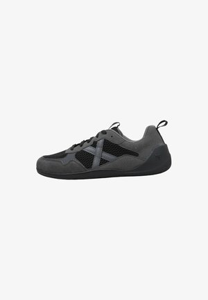 Zapatilla deportiva en gris oscuro y negro con paneles de malla, superposiciones de ante, cierre de cordones y tiradores en el talón y la lengüeta.