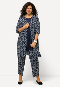 Navy-musterndes Outfit mit einem langen Cardigan mit weißen abstrakten Designs und passenden lockeren Hosen, kombiniert mit einem einfarbigen marineblauen Oberteil und schwarzen Ballerinas.