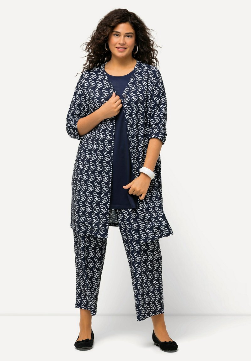 Navy-musterndes Outfit mit einem langen Cardigan mit weißen abstrakten Designs und passenden lockeren Hosen, kombiniert mit einem einfarbigen marineblauen Oberteil und schwarzen Ballerinas.