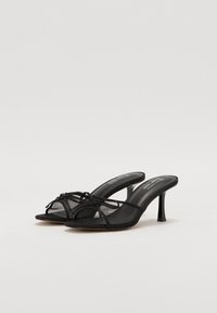 Zwarte schoenen met hakken gemaakt van synthetisch materiaal, met gaasbandjes, ronde neus en strikdetails aan de voorkant. Slanke stiletto-hak.