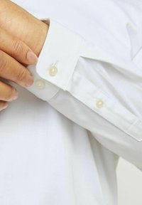 White dress shirt cuff featuring a single button closure and smooth fabric, with subtle stitching details and a classic fit design.