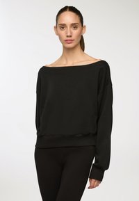 Felpa nera off-the-shoulder con vestibilità relaxed, polsini e orlo a coste. Realizzata in tessuto morbido con una texture liscia, abbinata a leggings neri.