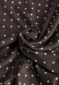 Tessuto marrone con una superficie liscia, caratterizzato da un motivo di pois bianchi distribuiti uniformemente. Il materiale è arricciato e piegato.