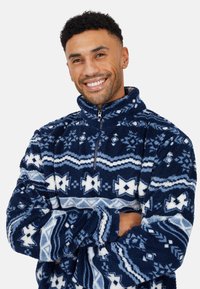 Pullover in pile blu navy con colletto alto, chiusura con zip a metà e motivi geometrici bianchi e azzurri in tutta la superficie. Texture morbida.