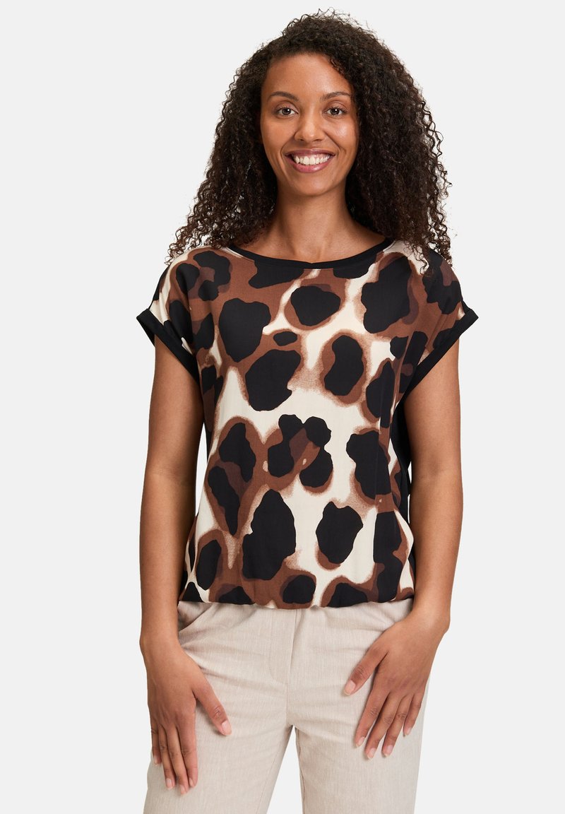 T-shirt à manches courtes, décontracté, avec un imprimé animal brun et noir sur fond crème. Tissu léger et lisse avec des accents noirs.