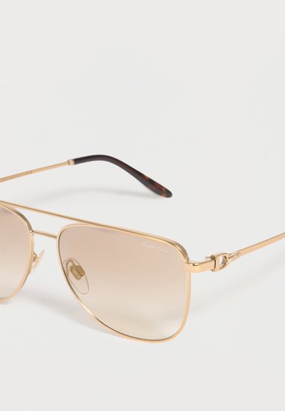 Αviator γυαλιά ηλίου με χρυσό μεταλλικό σκελετό, καφέ φακούς με βαθμιαία απόχρωση και μοτίβο χελώνας στα άκρα των βραχίονων σε λευκό φόντο.