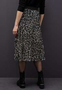 Plisovaná midi sukně z průhledného šedého materiálu s černým leopardím vzorem. Má černý pas a je doplněna kotníkovými botami.