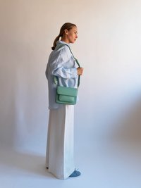 Lyseblå oversized skjorte, hvide vide bukser, mintgrøn crossbody taske og blå flade sko, med slank form og subtile accenter.