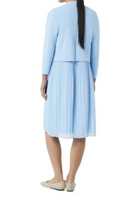 Jasnoniebieski kardigan nałożony na plisowaną jasnoniebieską sukienkę, z okrągłym dekoltem i rękawami do łokcia. Beżowe baleriny dopełniają strój.