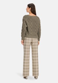 Olivegrüner, gestrickter Pullover mit einem strukturierten Rautenmuster; kombiniert mit beigen, karierte, weit geschnittenen Hosen in hellbraunen und dunklen Sandtönen.