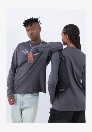 Hallide pikkade varrukatega särgid on kaunistatud peene graafikaga. Ühel modelil on seljas heledad teksapüksid; teisel on must õlakott logoga.