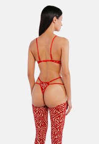 Rotes Bondage-Set mit dünnen Trägern, einem Cut-out-Design und zebra-musternden, knielangen Strümpfen aus einem transparenten Material.