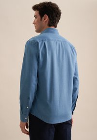 Lichtblauwe spijkerblouse met een klassieke kraag, knopenmanchet en een gebogen zoom. Gladde textuur, onversierde ontwerp, weergegeven vanaf de achterkant.