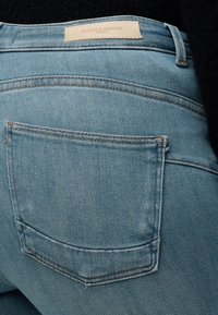 Πίσω τσέπη ανοιχτό μπλε τζιν με ορατή ραφή και μπεζ ετικέτα από δέρμα με την επωνυμία "Blue Denim Anno 1995 Only."
