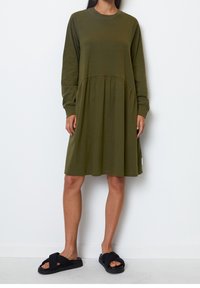 Kostium w oliwkowym kolorze z długimi rękawami, wyprofilowaną górą i plisowaną spódnicą. Materiał wydaje się miękki, ma okrągły dekolt i żadnych widocznych wzorów.