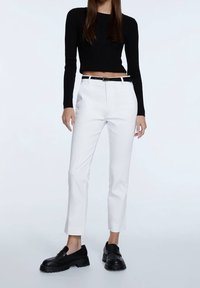 Pantalones blancos ajustados y una camiseta de manga larga de rayas negras. El conjunto se complementa con unos mocasines negros gruesos y un cinturón negro con una hebilla plateada.